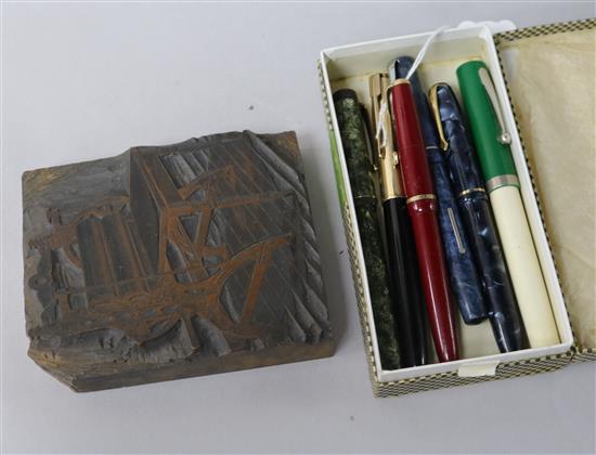 A woodblock carved with a printers press and various vintage fountain pens